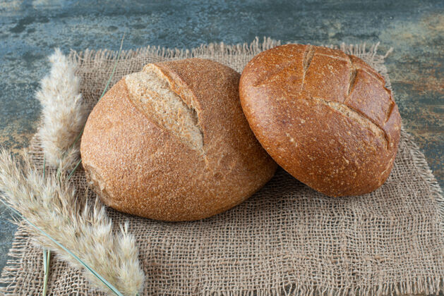 美味两个新鲜的棕色面包和麻布上的小麦美味小麦美味