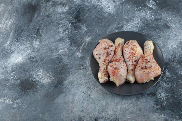 晚餐黑色盘子上的生腌鸡腿俯视图 背景为灰色烧烤生的深色