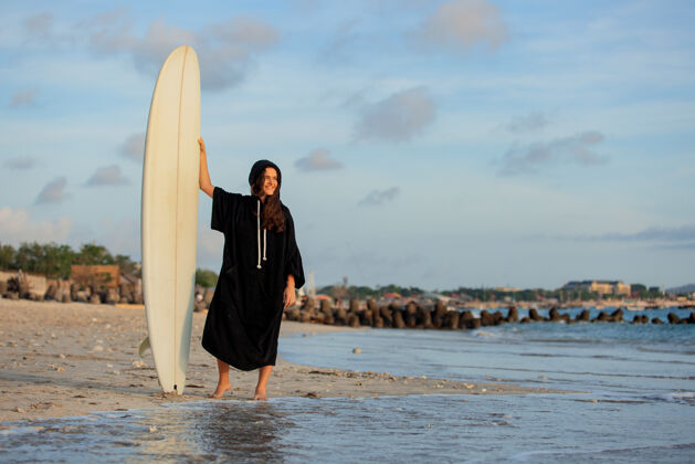 冲浪者美丽的女孩拿着冲浪板站在沙滩上女性热带活跃的女孩