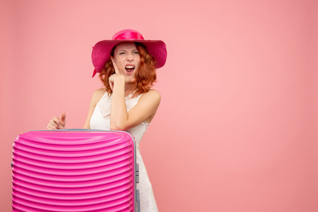 度假粉色墙上带着粉色包的女游客正面图航行美丽帽子