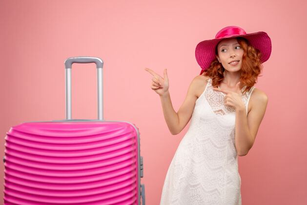 情感年轻的女性游客与粉红色的帽子和粉红色的墙壁上的包的正面视图快乐旅行精品