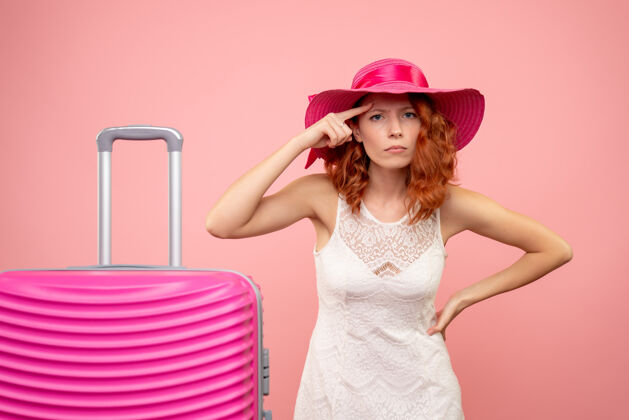 夏天年轻的女性游客与粉红色的帽子和粉红色的墙壁上的包的正面视图时尚前面帽子