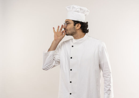 眼镜站在剖面图年轻的男厨师穿着厨师制服和眼镜显示美味的姿态隔离在白色的墙壁上视图男性烹饪