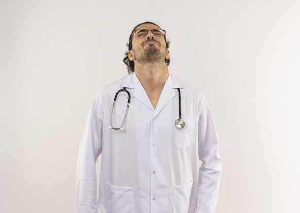 眼镜年轻的男医生 戴着眼镜 穿着白色长袍 戴着听诊器 闭着眼睛 在隔离的白色墙壁上抬起头 留着复印空间医生光学提高