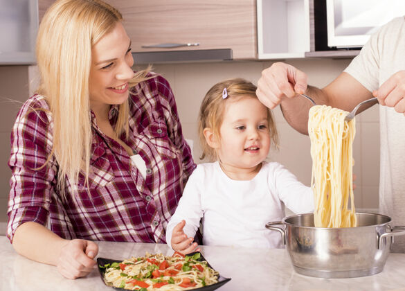 烹饪快乐家庭和他们的小女儿在厨房柜台上准备自制意大利面室内柜台女人
