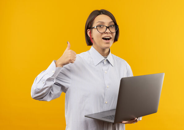 眼镜印象深刻的年轻呼叫中心女孩戴着眼镜拿着笔记本电脑显示拇指向上孤立的橙色年轻笔记本呼叫