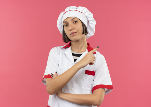 壁板自信的年轻女厨师身着厨师制服 站在封闭的姿势 指着粉红色的一侧 留有复印空间信心复制粉色