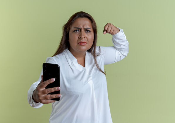 随意严格随意的白人中年女子手持电话 表现出强烈的姿态孤立在橄榄绿的墙上握着强壮女人