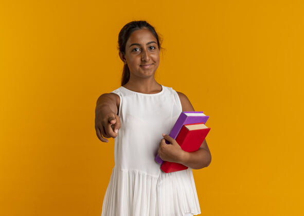 抱着高兴的小女生拿着书 在橙色的墙上给你们看动作女学生年轻