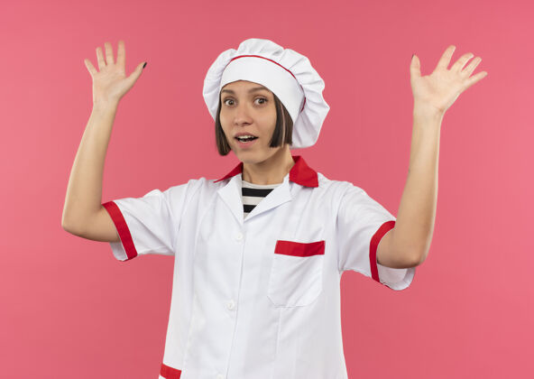 女印象深刻的年轻女厨师在厨师制服举起手孤立在粉红色印象制服年轻