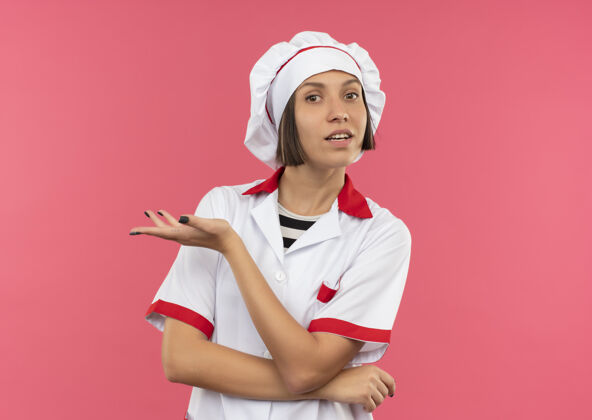印象令人印象深刻的年轻女厨师穿着厨师制服站在与封闭的姿态和显示空的手孤立在粉红色的复制空间复制显示粉色
