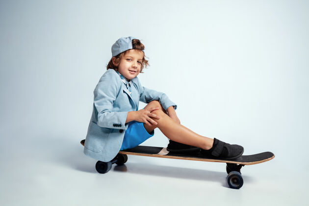 欢呼漂亮的小男孩在滑板上穿着休闲服在白色的工作室衬衫情感孩子