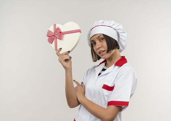 烹饪印象深刻的年轻女厨师在厨师制服举行心形礼品盒上白色的复制空间隔离复制年轻厨师