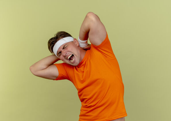腕带疼痛的年轻英俊的运动型男子戴着头带和腕带把手放在脖子后面的橄榄绿与复制空间隔离橄榄穿脖子