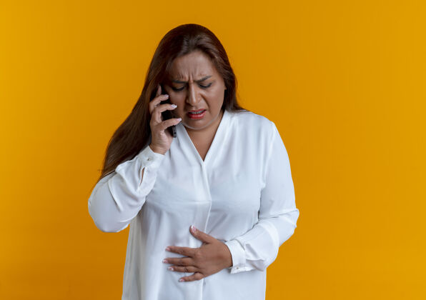 胃一个生病的白人中年妇女正在打电话 把手放在隔离在黄色墙壁上疼痛的胃上女人生病疼痛