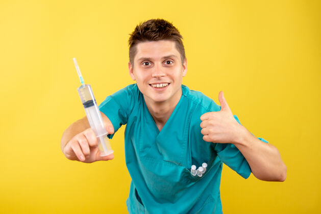 微笑正面图身着医疗服的年轻男医生拿着黄色背景上的针剂医学注射西装