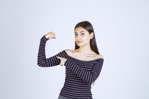 力量穿着条纹衬衫的年轻女子展示她的手臂肌肉和拳头人类幸运姿势
