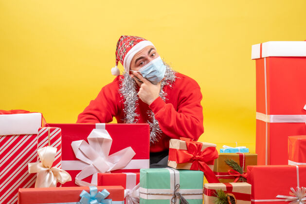 病毒正面图：年轻男性围坐在黄色背景上 戴着面具展示礼物坐着流行病圣诞节