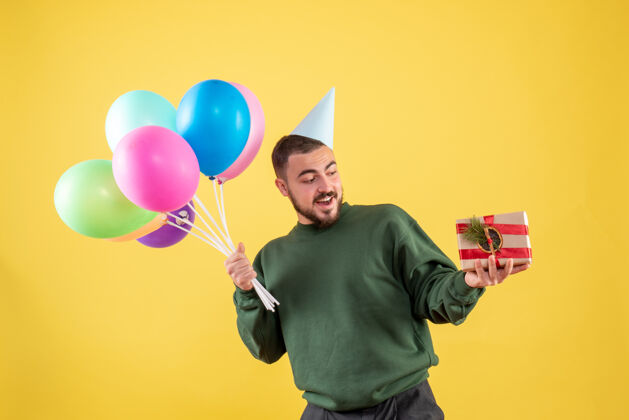 生日正面图：手持彩色气球的年轻男性 背景为黄色年轻男性气球背景