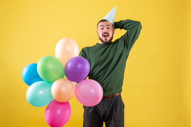 庆祝正面图黄色背景上有彩色气球的年轻男性背景购物生日