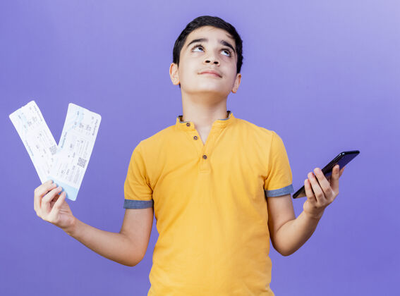 持有一个体贴的白人小男孩 手里拿着机票和手机 孤零零地仰望着紫色的背景思想男孩手机