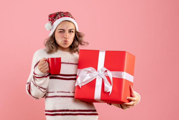 情感年轻的女性拿着圣诞礼物和一杯粉红色的茶杯子粉色丝带