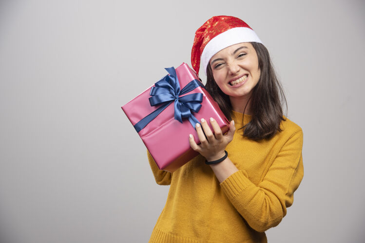 年轻戴着圣诞帽拿着礼品盒的快乐女人漂亮庆祝圣诞老人