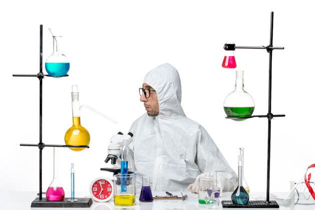 科学正面图穿着特殊防护服的男科学家围坐在办公桌旁 拿着解决方案化学烧杯周围