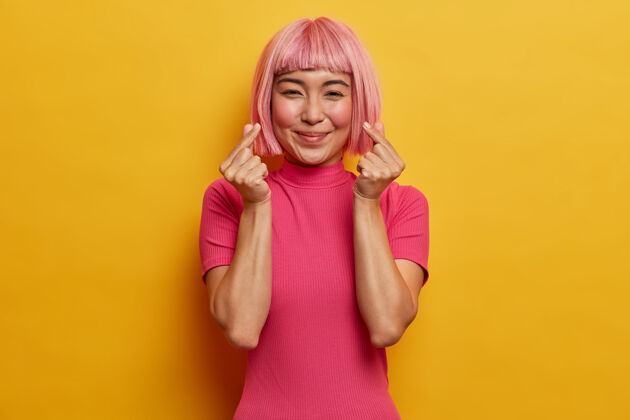 请温柔微笑的漂亮女人 时尚的粉色发型 做出韩式手势 表达爱 心情愉快浪漫高兴粉色