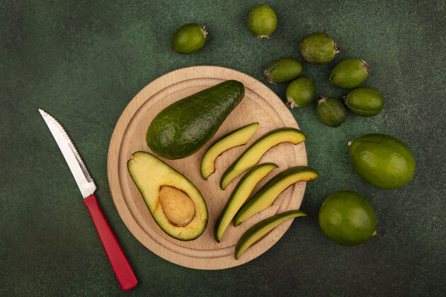 膳食绿皮鳄梨的俯视图 切片放在木制的菜板上 刀子上夹着酸橙和柠檬 隔离在绿色的墙上食物素食者皮