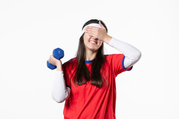 哑铃正面图穿着运动服的年轻女性在白墙上用哑铃锻炼球员前面观点