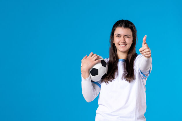 肖像前视图：蓝色墙上有足球的年轻女性比赛人物年轻女性
