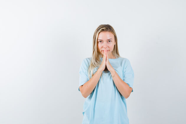 时尚金发女孩抱在祈祷的立场在蓝色t恤 看起来很漂亮 前视图双手年轻前面手