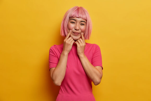 力量性感积极的粉红头发女士 手指靠近嘴角 强颜欢笑 假装心情很好时尚粉色假发有趣