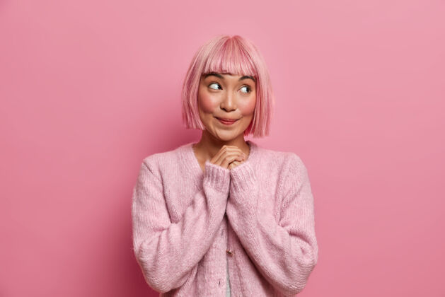 思想梦幻靓女室内照有粉色短发 表情开心满意的一边看 双手合十 穿套头衫粉色假发模特梦幻
