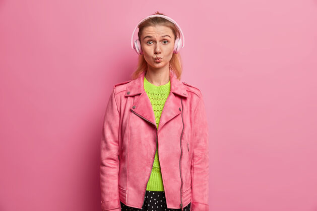 满意有趣的欧洲女孩嘴唇圆润 戴着耳机听音乐 在播放列表中选歌 在上学的路上 穿着时髦的粉色夹克 喜欢最喜欢的歌手爱好数码白种人
