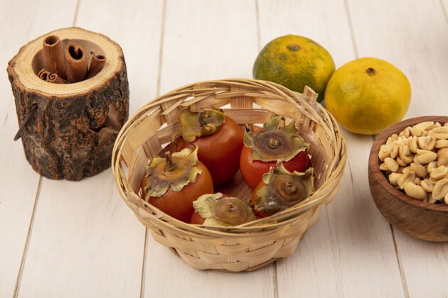 柿子新鲜柿子放在木桶里 花生放在木碗里 橘子被隔离在白色的木墙上食物桶风景