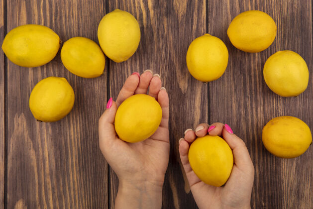切片女性手拿新鲜柠檬的顶视图 柠檬被隔离在木墙上配料块持有