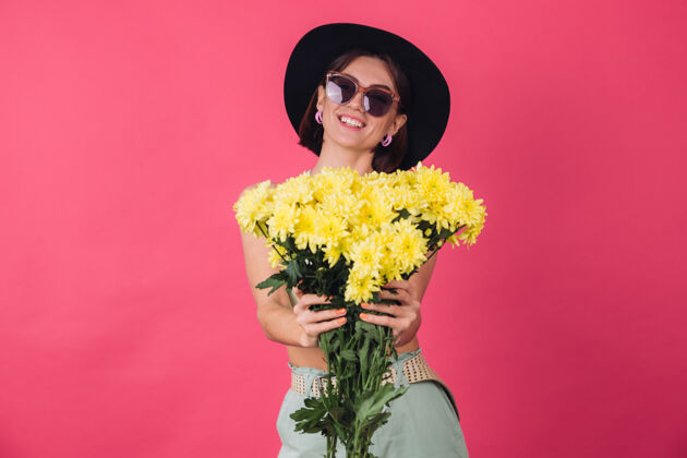 植物学漂亮时尚的女人戴着帽子和墨镜摆姿势 捧着一大束黄紫苑 春意盎然 积极向上的情绪与世隔绝花店无忧无虑深色