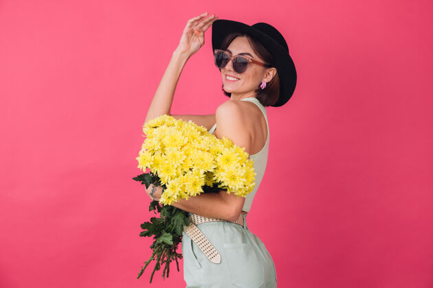 成人漂亮时尚的女人戴着帽子和墨镜摆造型 捧着一大束黄紫苑 春意盎然 积极向上的情感与世隔绝庆祝香味肖像