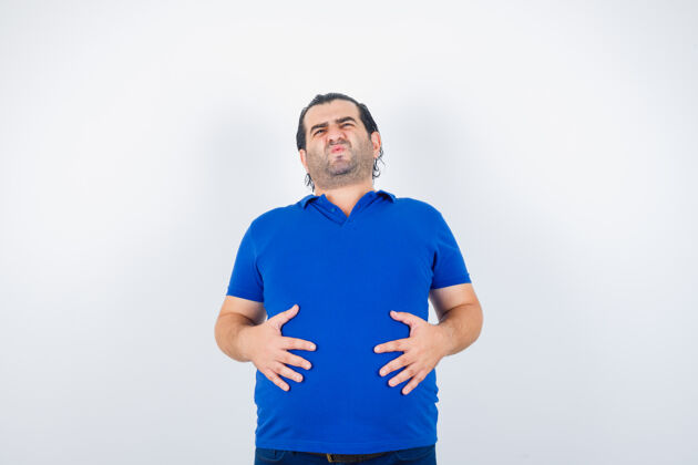 症状身穿蓝色t恤的中年男子 手放在肚子上 看起来不舒服 正面视图生病男性发烧