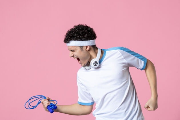 锻炼正面图：穿着运动服的年轻男性 粉色墙上挂着跳绳成功耳机粉红