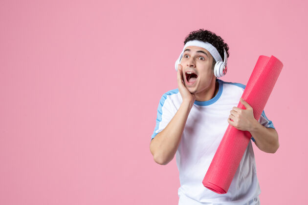 人正面图穿着运动服的年轻男性 粉色墙上有瑜伽垫垫子视图健身房