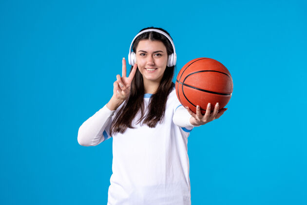 人正面图：戴着耳机拿着篮球的年轻女性站在蓝色的墙上球胜利前面
