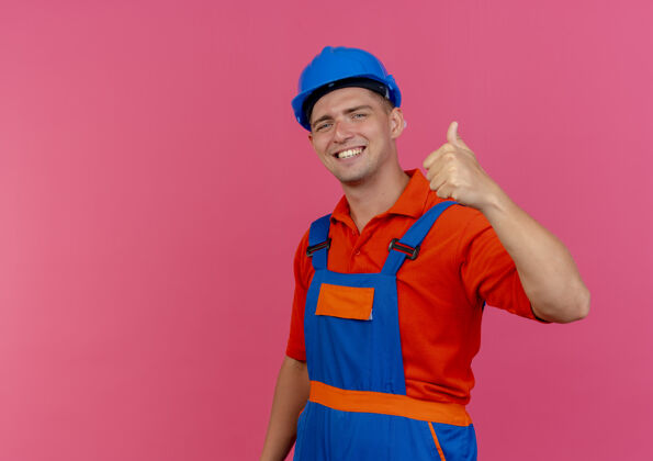空间微笑着的年轻男性建筑工人穿着制服 戴着安全帽 大拇指朝上放在粉红色的地板上男性复制年轻