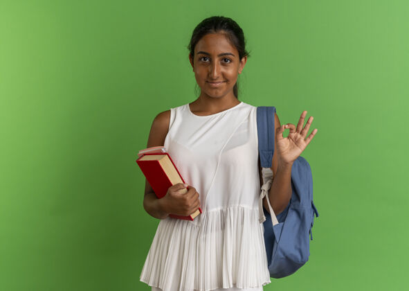 女学生高兴的小女生背着书包拿着带笔记本的书 在绿色的草地上摆出一副好姿势笔记本包背