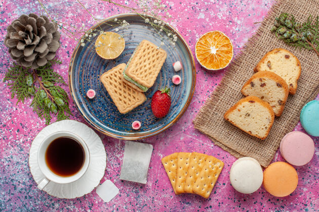 烘焙美味的华夫饼和麦卡龙的俯视图 粉色表面上有一杯茶饼干餐派