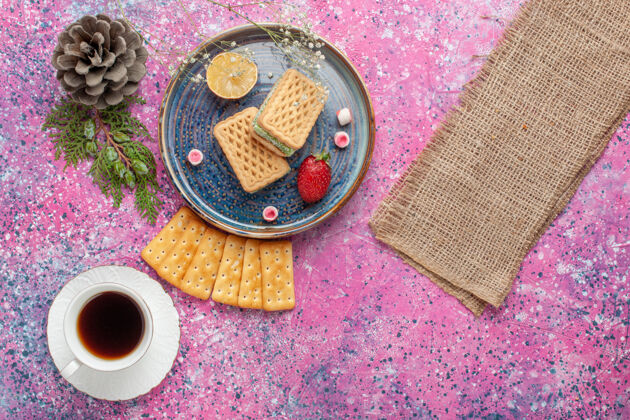 麦卡龙美味的华夫饼和法式麦卡龙饼干的俯视图 粉红色的表面上放着茶杯子法国食物