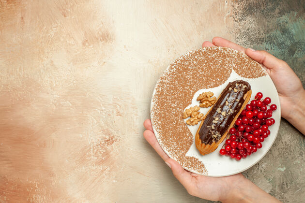 顶部俯瞰美味的eclair与红色浆果放在一张清淡的桌子上甜甜的蛋糕甜点食物多汁健康