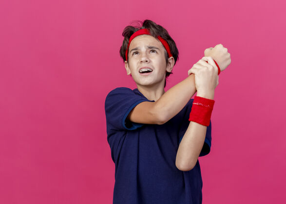 市民年轻帅气的运动男孩 戴着头带和护腕 戴着牙套 抬起头来 把手腕隔离在深红色的墙上牙齿运动头带